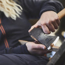 Person using HULTAFORS Agelsjon Mini Hatchet to carve wood, showing compact carbon steel blade and wooden handle.