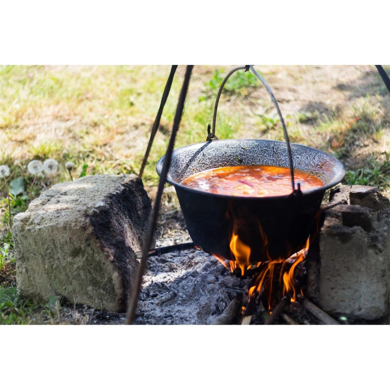 Enameled Dutch oven hanging over campfire cooking stew outdoors with stones supporting the firepit