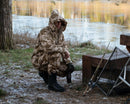 Person wearing Genuine British army desert camouflage combat trousers crouching by a lakeside in outdoor setting.