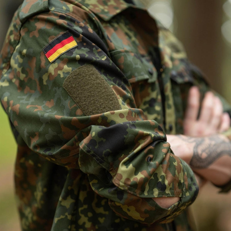Close-up of a person wearing Leo Kohler tactical military shirt in flecktarn camouflage with German flag patch on sleeve