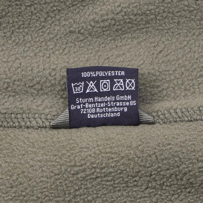 Close-up of MIL-TEC army style fleece jacket label showing 100% polyester material and care instructions on olive fabric
