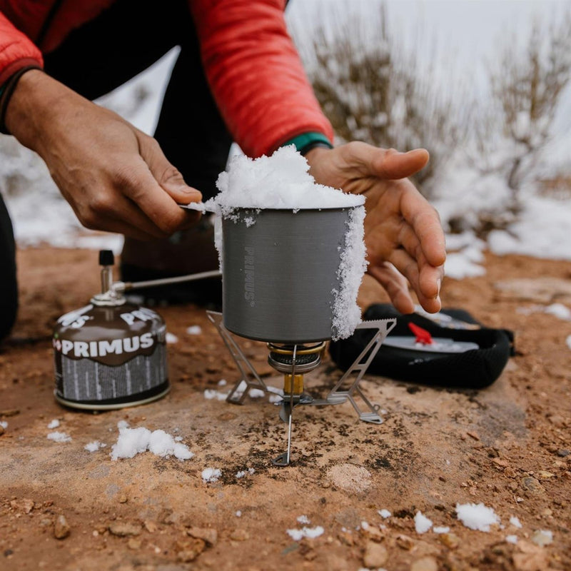 Hand adding snow to pot on Primus Express Spider II tripod camping stove outdoors in cold weather