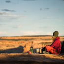 Person sitting near outdoor campsite with Primus PrimeTech 2.3L cooking set preparing a meal in nature.