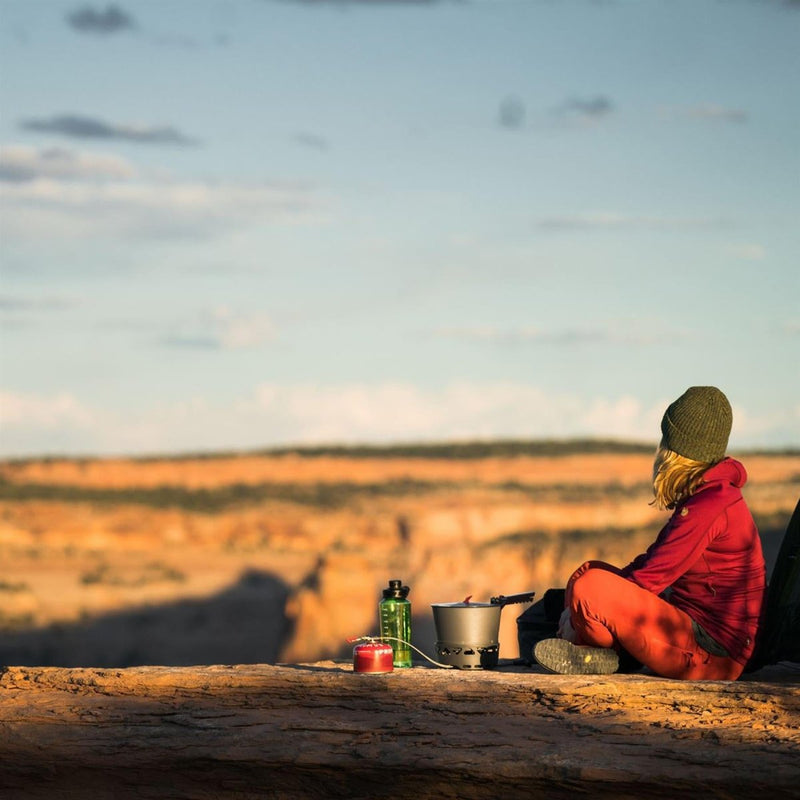 Person sitting near outdoor campsite with Primus PrimeTech 2.3L cooking set preparing a meal in nature.